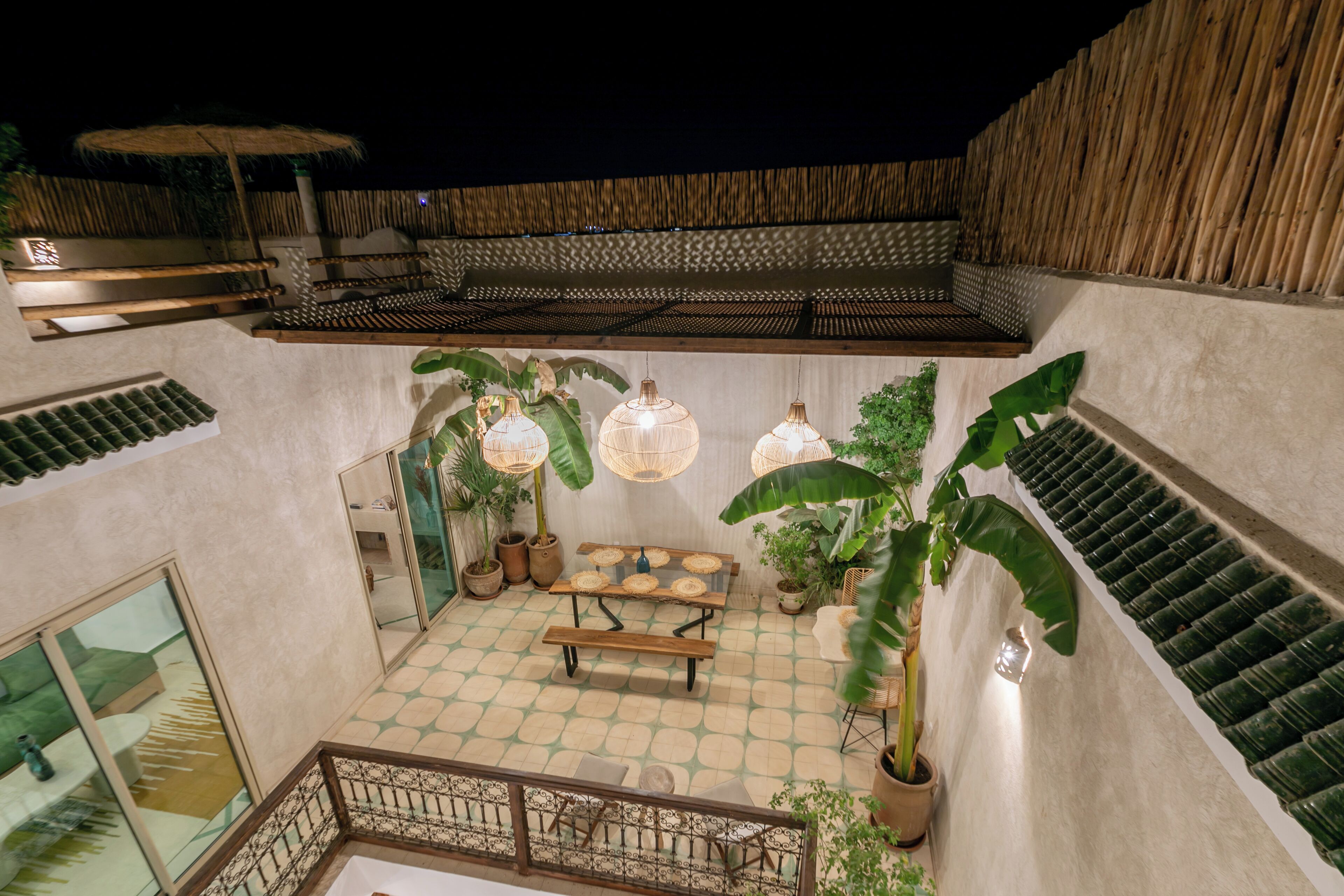 A rooftop terrace with a checkered floor, a wooden bench, hanging lanterns, and potted plants.