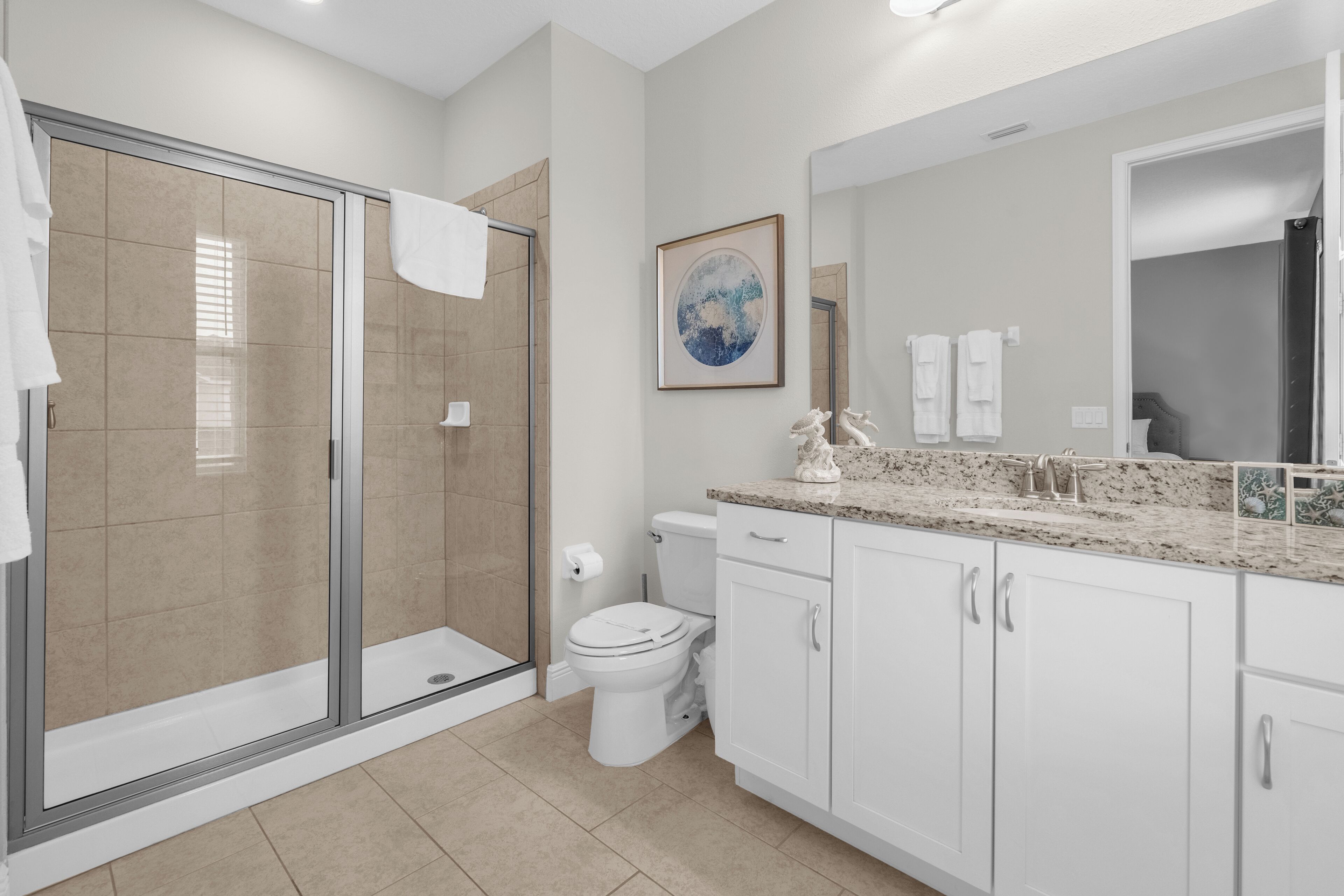 A modern bathroom with a glass shower enclosure, a toilet, and a sink with a granite countertop.