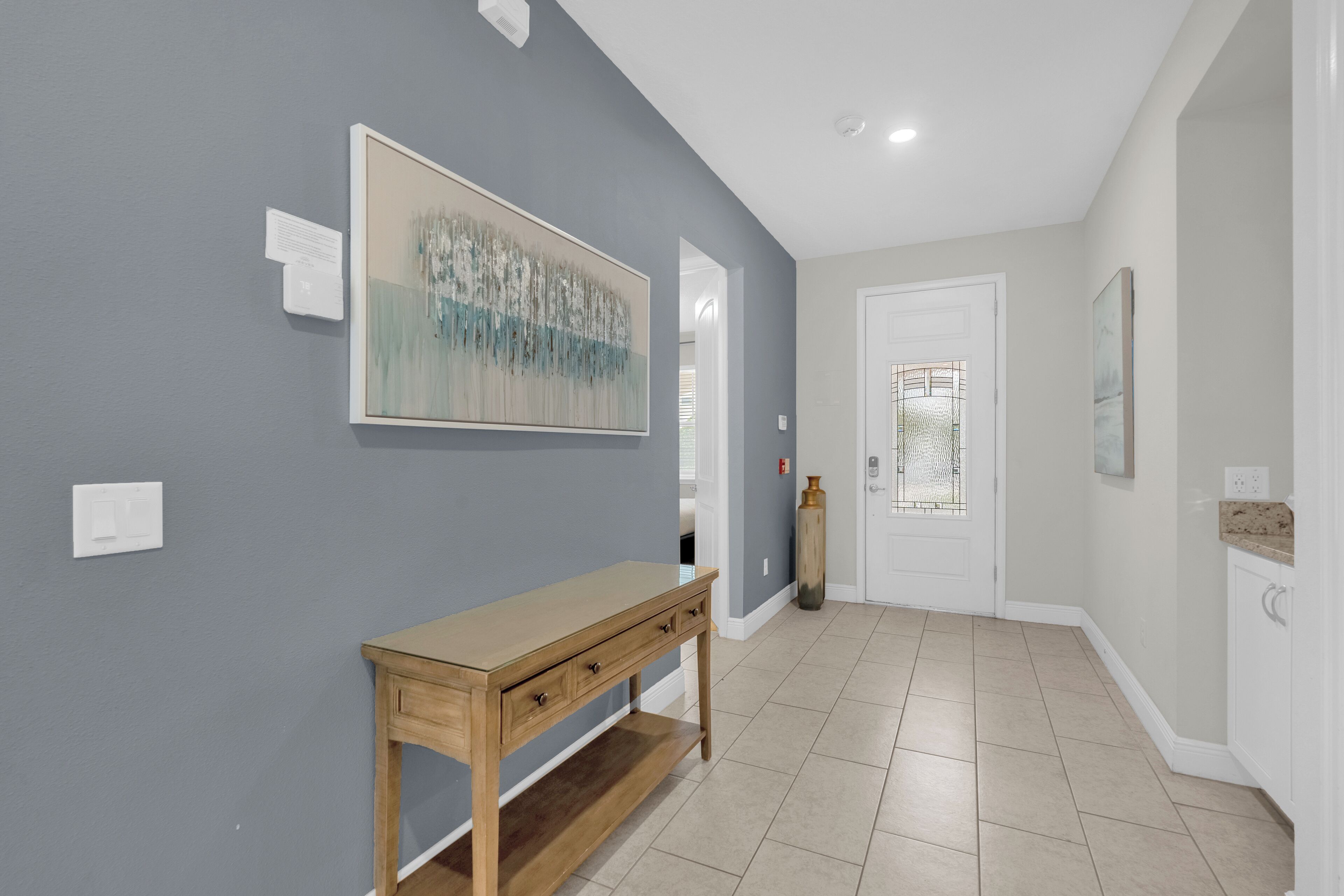 A hallway with a wooden bench, a painting on the wall, and a door with a glass panel.