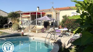 Un área de piscina con un porche cubierto, mobiliario exterior y una parrilla.