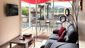 Una sala de estar con un sofá, una mesa de centro, un televisor y un balcón con una sombrilla roja.