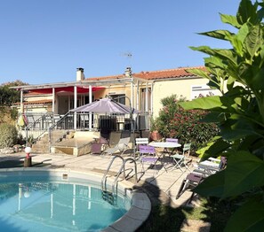 Ein Poolbereich mit überdachter Terrasse, Sitzgelegenheiten im Freien und einem Grill.
