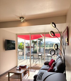 Ein Wohnzimmer mit einer Couch, einem Couchtisch, einem Fernseher und einem Balkon mit einem roten Sonnenschirm.