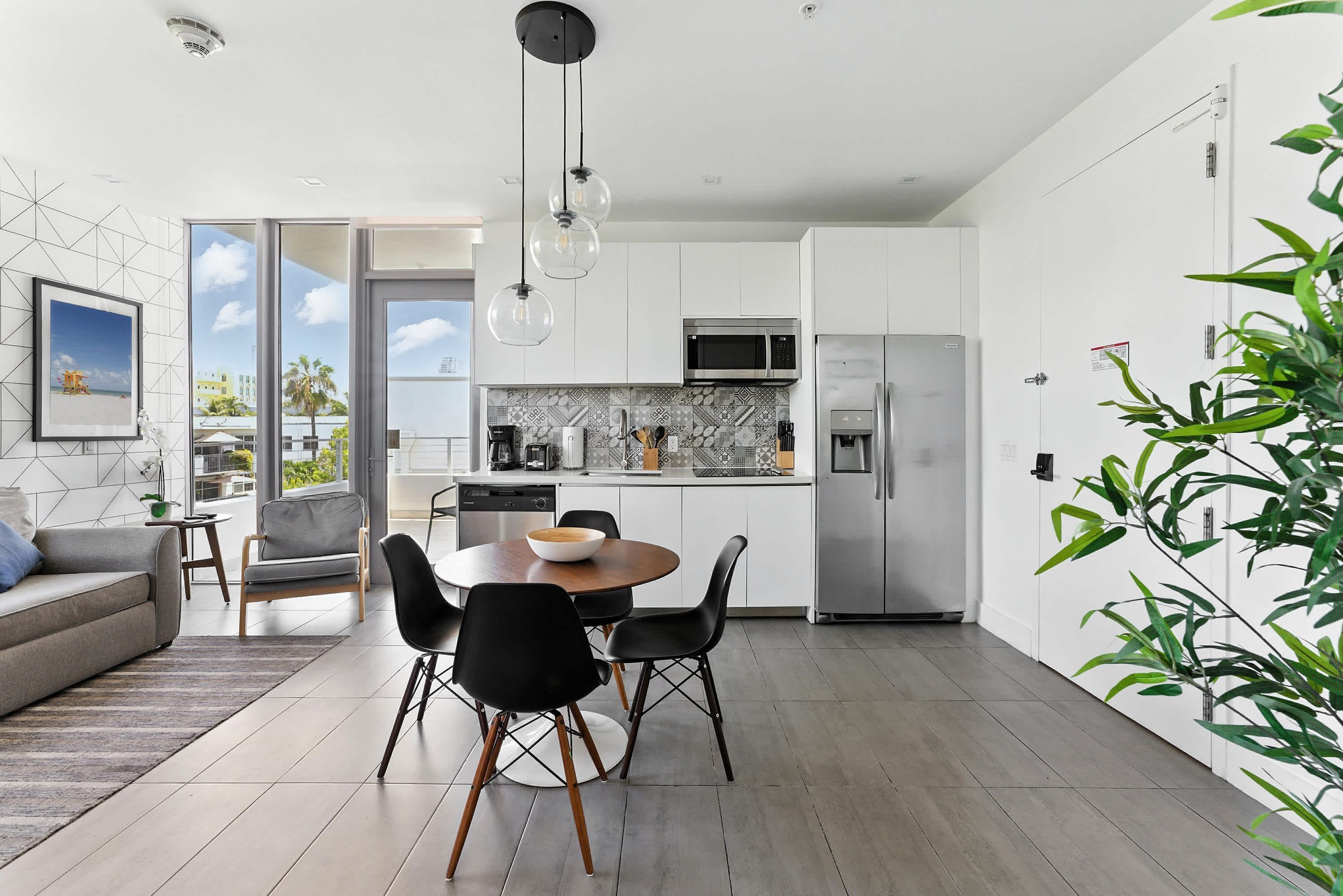 A modern kitchen with white cabinets, a stainless steel refrigerator, and a dining area with a round table and black chairs.