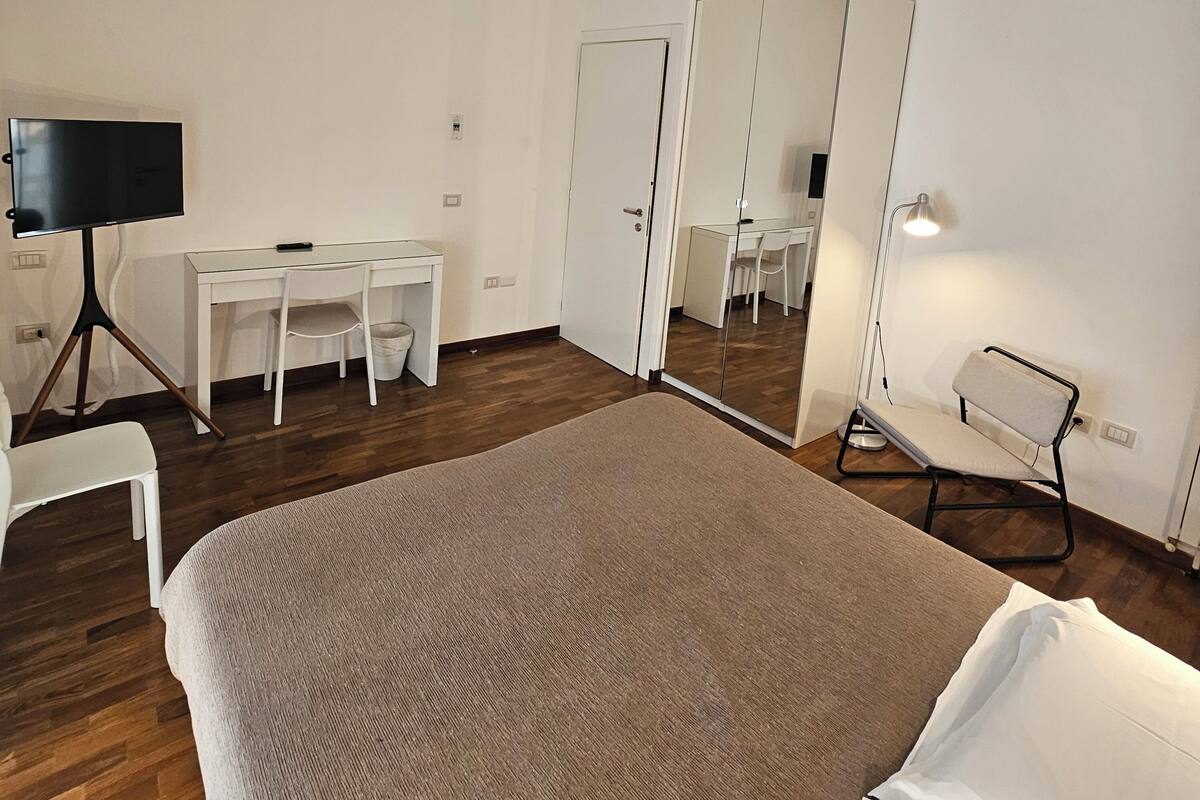 Ein Schlafzimmer mit einem Bett, einem Schreibtisch, einem Stuhl, einem Kleiderschrank und einem Spiegel.