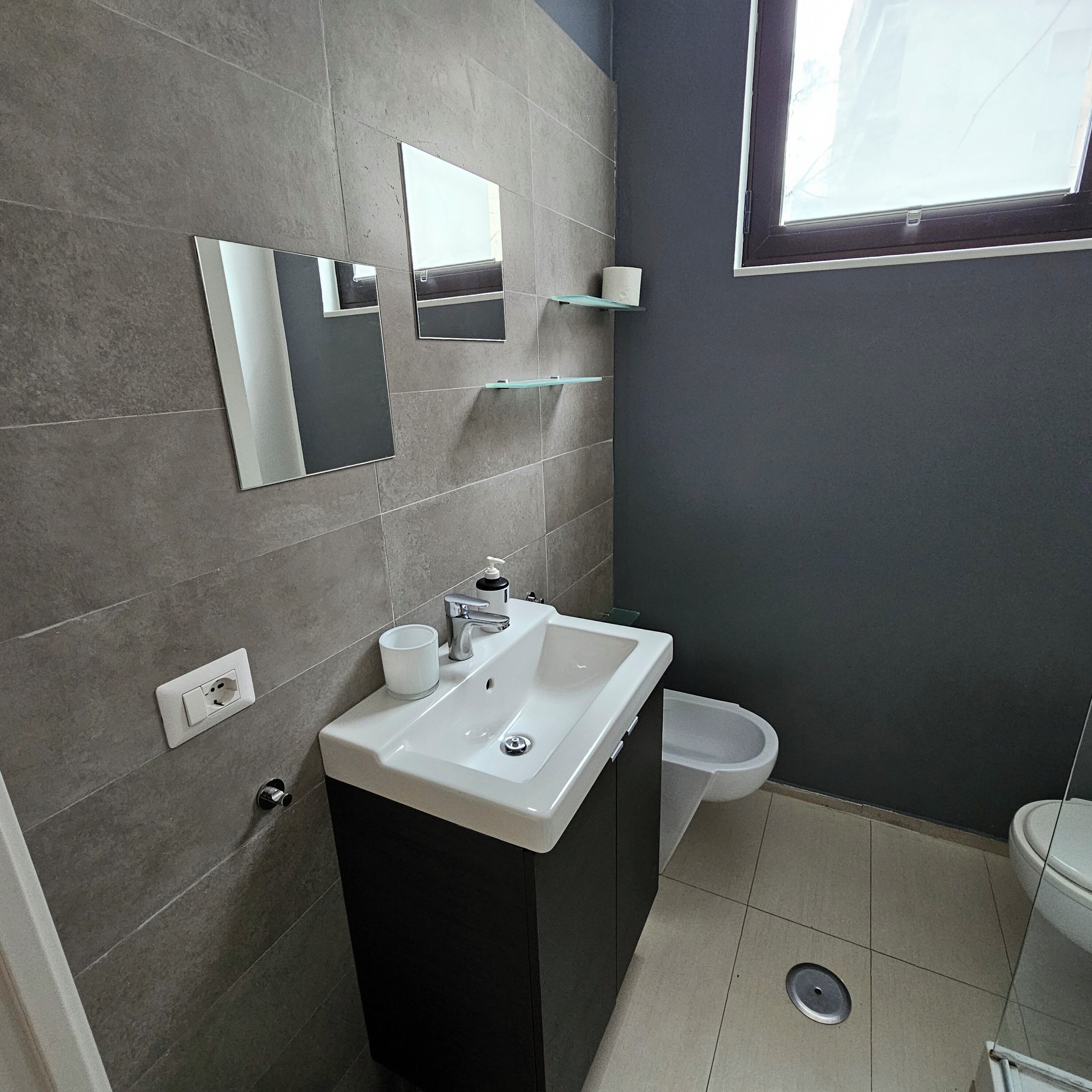 Uma casa de banho moderna com uma sanita, um lavatório branco e um espelho.