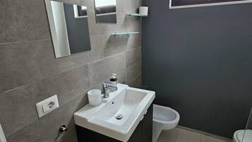 Uma casa de banho moderna com uma sanita, um lavatório branco e um espelho.