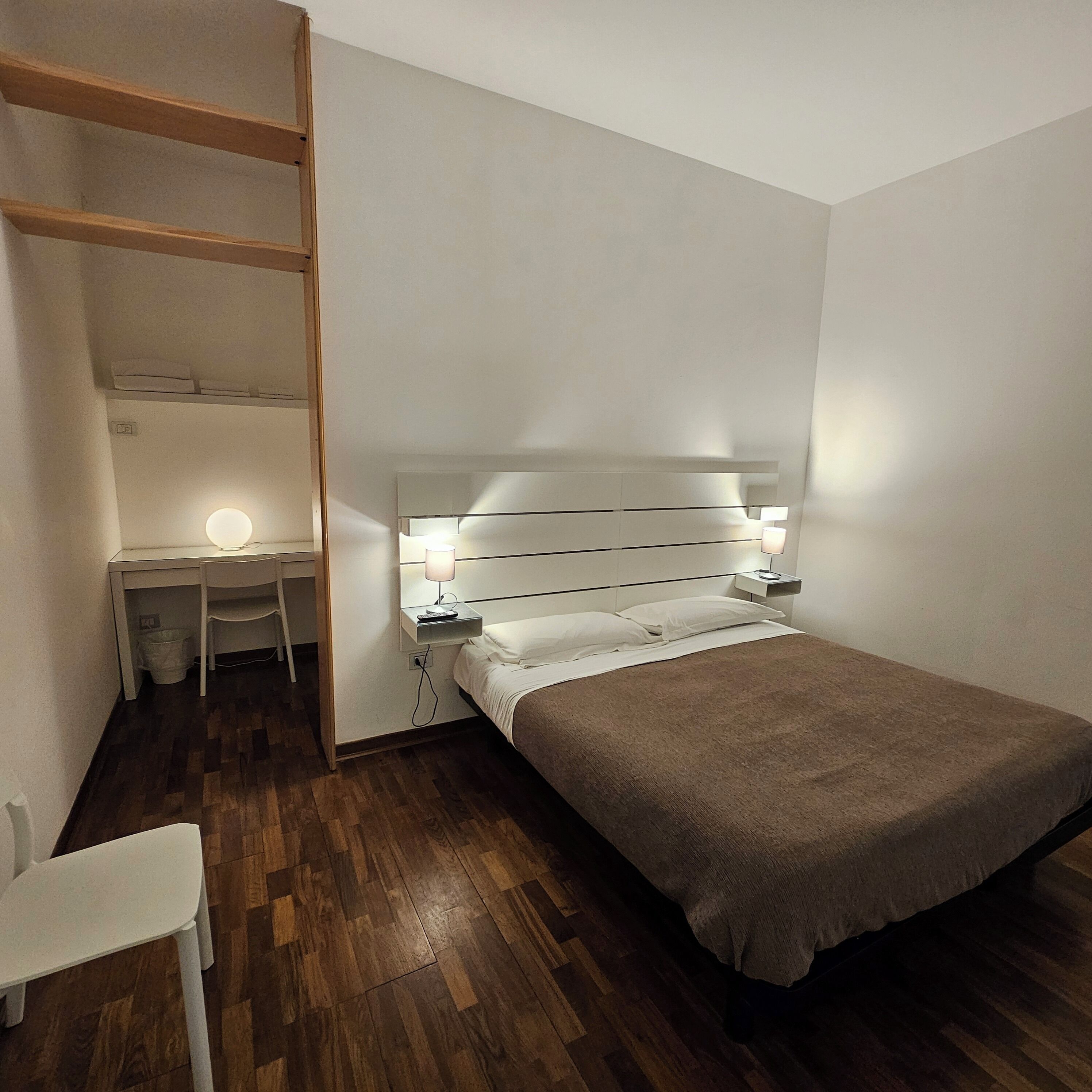 A small, neatly arranged bedroom with a single bed, a desk, and a chair.