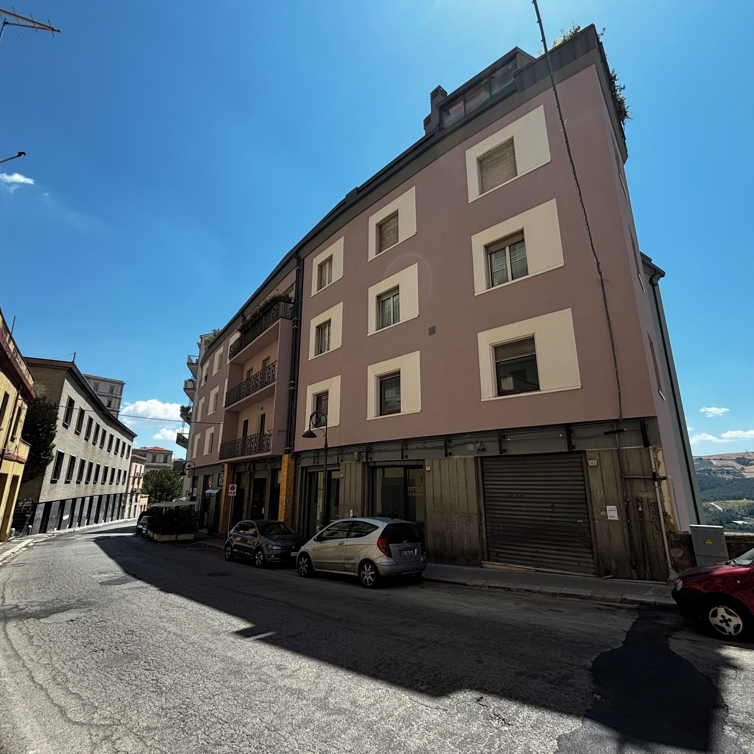 A multi-story building with a ground-floor shop and parked cars.