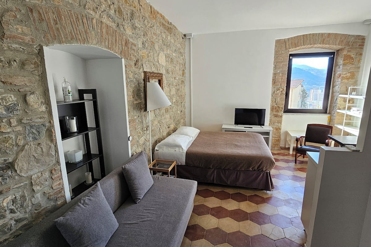 Ein Zimmer mit Steinstruktur, einer Couch, einem Bett, einem Fernseher und einem Fenster mit Blick.