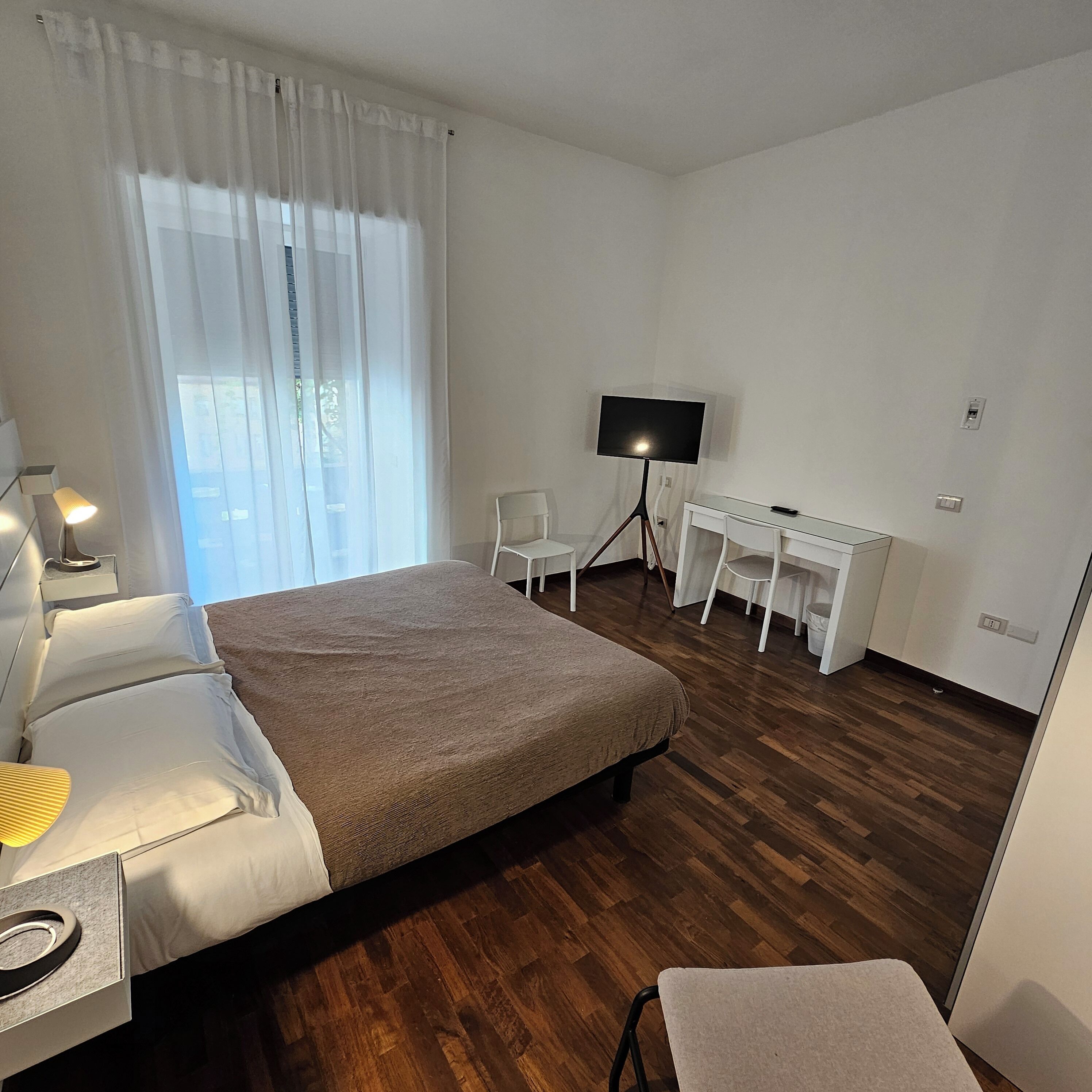 A hotel room with a bed, a desk, a chair, a TV, and a window with curtains.