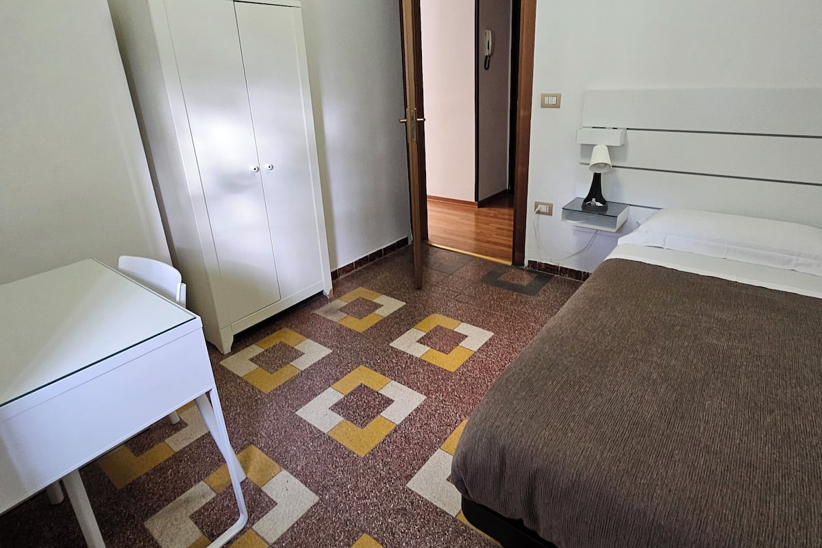 Ein Schlafzimmer mit Bett, Schreibtisch, Kleiderschrank und einem gemusterten Teppich.