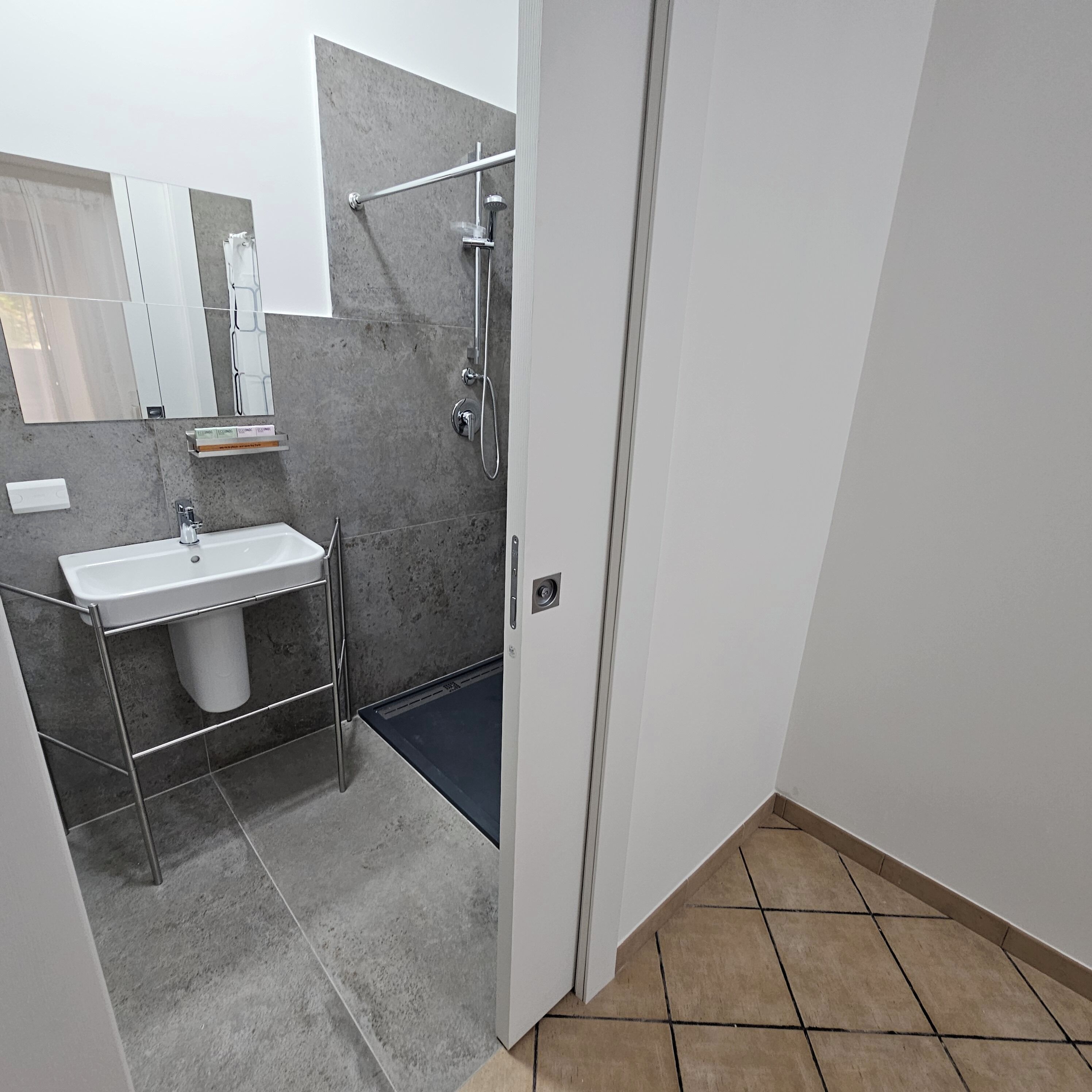 A modern bathroom with a white sink, a mirror, and a shower area.