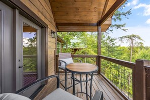 Eine Holzdielen-Terrasse mit Tisch, Stühlen, einer Tür und Blick auf Bäume.