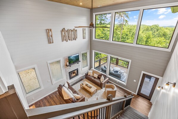 A spacious living area with a fireplace, large windows, and a view of the outdoors. - Smoky Cove Splash: 5-bedroom Pool cabin close to the action of Pigeon Forge (Sevierville)