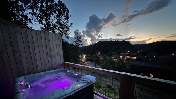 Un jacuzzi en una terraza de madera con vista a un pueblo y montañas al fondo.