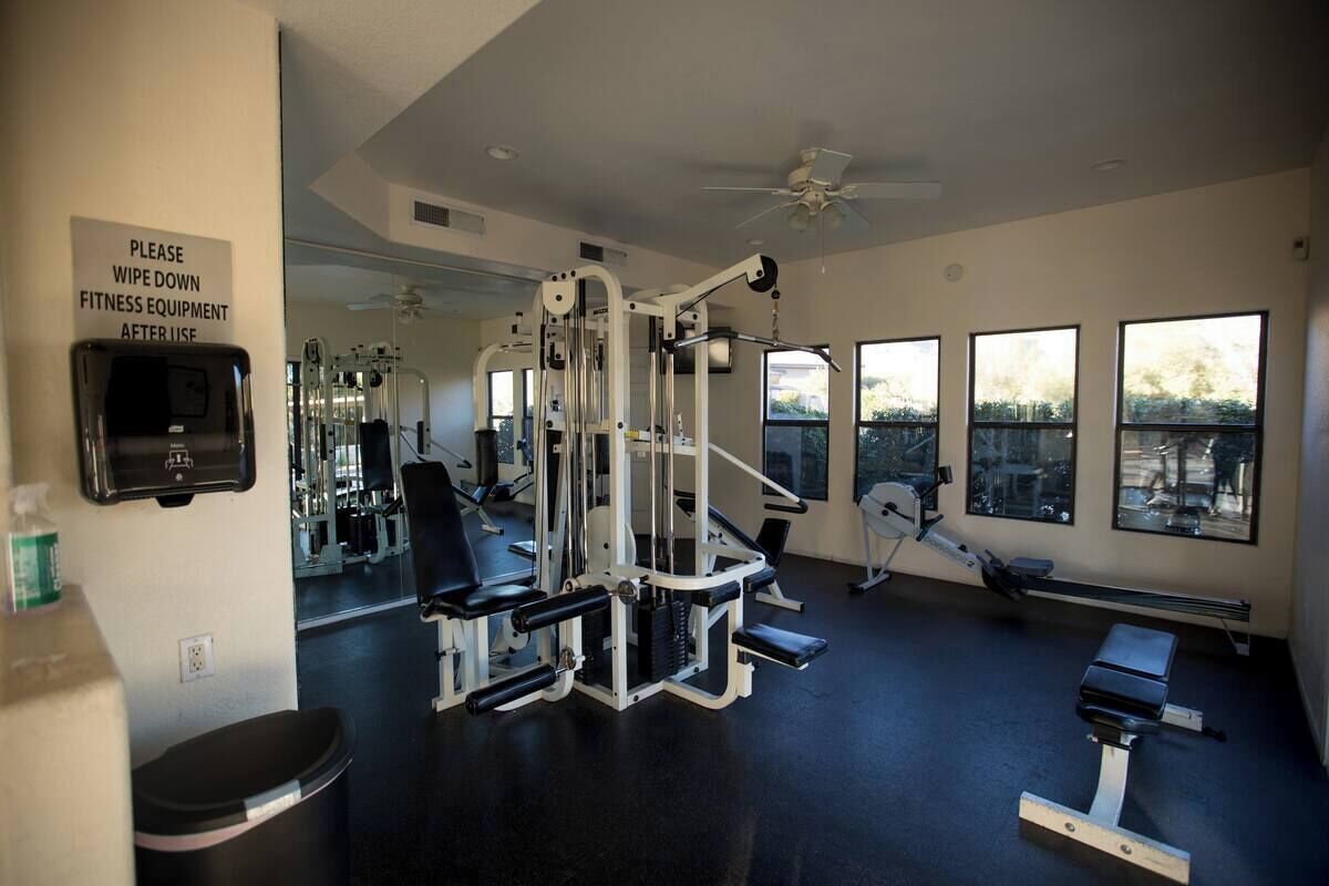 A gym with exercise equipment, a sign instructing to wipe down equipment, a ceiling fan, and large windows with a view.