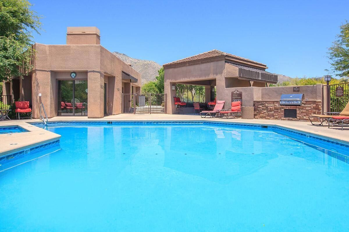 A swimming pool with red lounge chairs and a barbecue area.