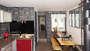 A modern kitchen with red cabinets, a black backsplash, and a wooden dining table with wine bottles and glasses.