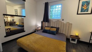A bedroom with a bed, a nightstand, a mirror, a window with curtains, and a framed picture on the wall.