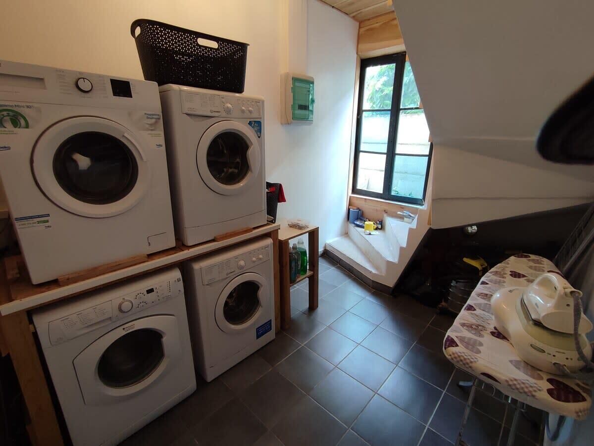 A laundry room with stacked washing machines, a small table with a kettle, and a window providing natural light.