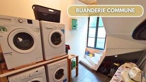 A laundry room with four stacked washing machines, a drying machine, and a table with an ironing board.