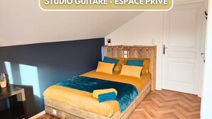 A private studio guitar room with a bed, wooden headboard, and a small table with a plant.