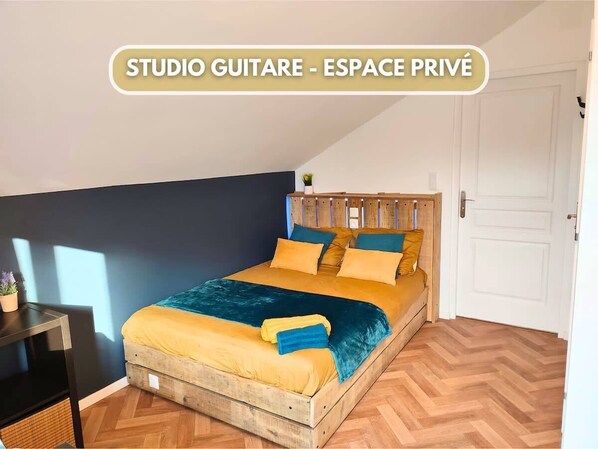 A private studio guitar room with a bed, wooden headboard, and a small table with a plant. - Guitar Studio - Music in Champagne (Châlons-en-Champagne)