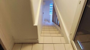 Eine schmale Treppe mit weißen Wänden und einem hölzernen Geländer, die zu einem Raum mit einem Fenster führt.