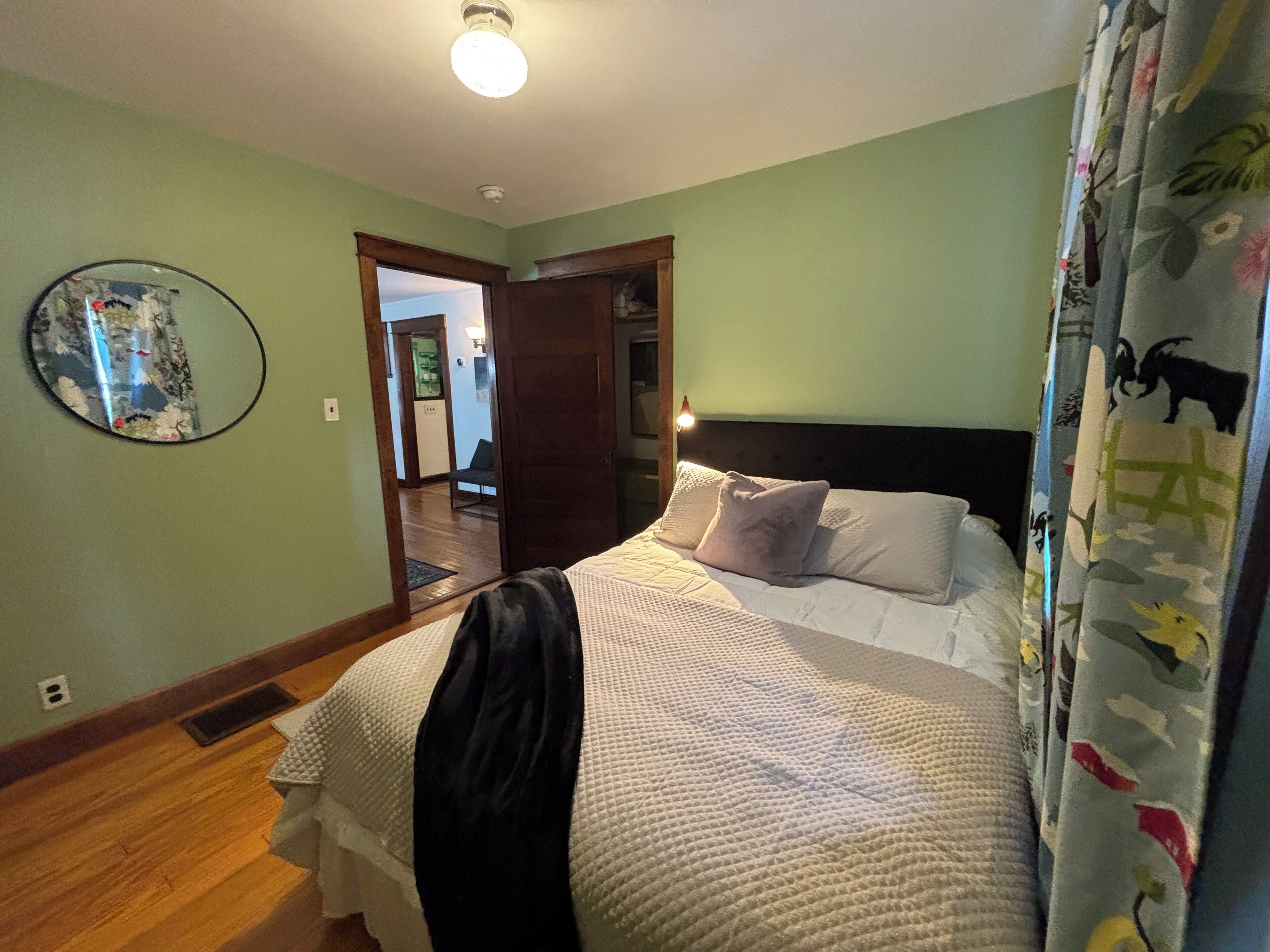 A bedroom with a bed, a headboard, a mirror, and a door leading to another room.