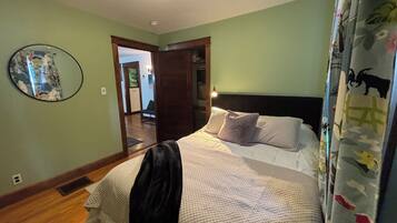 A bedroom with a bed, a headboard, a mirror, and a door leading to another room.
