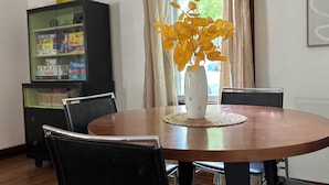 Een eethoek met een ronde houten tafel, zwarte stoelen, een witte vaas met gele bloemen en een zwart kastje met glazen deuren.
