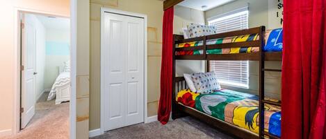 Un lit superposé avec une literie aux couleurs vives, une porte blanche et un rideau rouge.