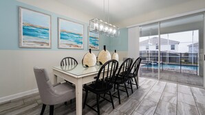 A dining area with a glass table, black chairs, and a view of a swimming pool through large glass doors. - 9BR Villa Home Theater Pool Sleeps 16 (Davenport)