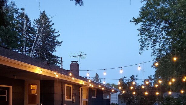 Een huis met een terras, buitenmeubels en lichtjes.