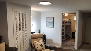 Een woonkamer met een bruine leren bank, een beige fauteuil met kussen, een houten salontafel en een kamerkleed met dessin. Op de witte muur hangt een ingelijst kunstwerk en het witte plafond heeft inbouwspots.