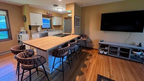 Een moderne keuken met een centraal eiland, barstoelen, een grote televisie en een eethoek.