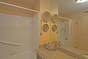 A bathroom with a white bathtub, a shower, and a vanity with a granite countertop. There are decorative woven baskets on the wall and a towel rack.