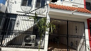 Un edificio de dos pisos con fachada blanca, tejado de tejas rojas y una verja de metal negro.