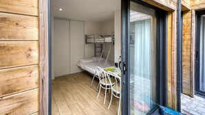 Habitació compacta amb un llit doble, una taula petita amb cadires i una porta corredissa de vidre que dona a una zona exterior.