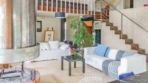 A spacious living area with a large cylindrical sculpture, a staircase, and a modern sofa set.