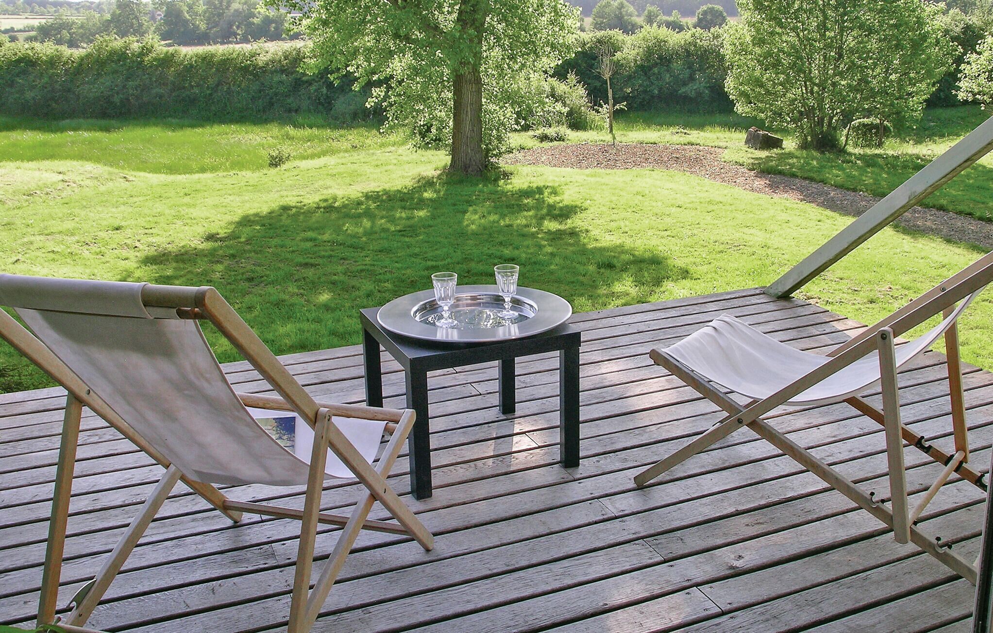 A wooden deck with two fold-out chairs and a small table with glasses.