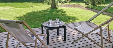 A wooden deck with two fold-out chairs and a small table with glasses.