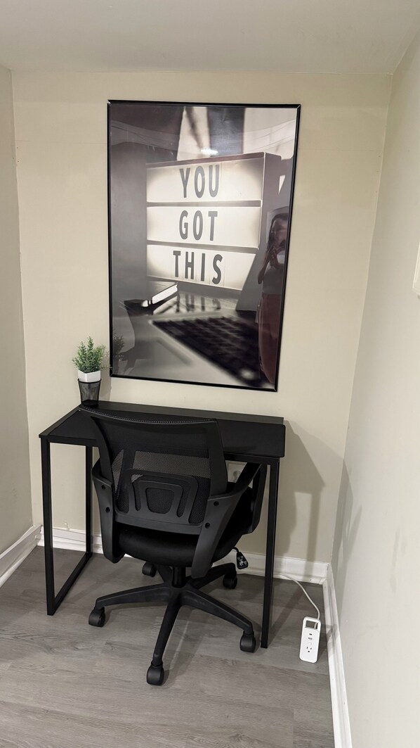 A desk with a computer, a potted plant, and a motivational poster on the wall.
