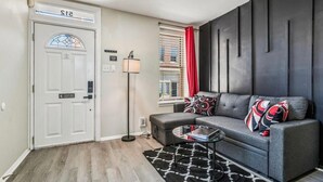 A modern living room with a grey sofa, a small coffee table, a floor lamp, and a patterned rug. - Camden's Little Charm-Walking Distance Stadium & Convention, University of MD (Baltimore)