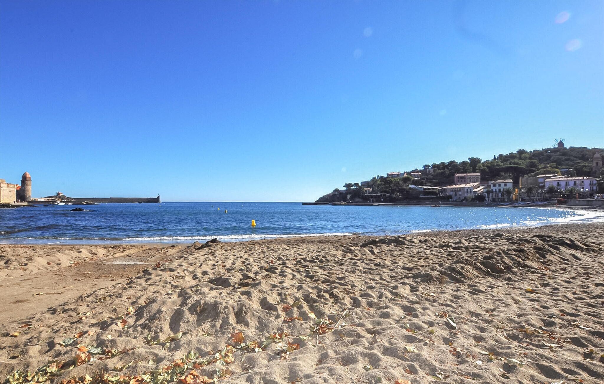 A beach with a clear sky, sandy shore, and buildings in the background.