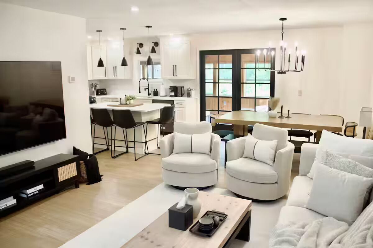 Un salon moderne avec un téléviseur à écran plat, une table basse et deux fauteuils blancs.