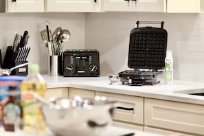 A kitchen with a waffle maker, a radio, and various utensils on the counter. - Modern Creekside Lakehouse (Ashville)