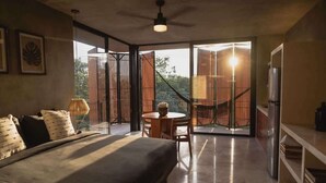A bedroom with a bed, a desk, and a chair, a balcony with a view of the outside, and a ceiling fan.