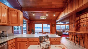 A wooden kitchen with a large island, wooden cabinets, and a view of mountains through the windows. - Paradise cove - A Mid-Century Modern Waterfront Retreat (Ketchikan)